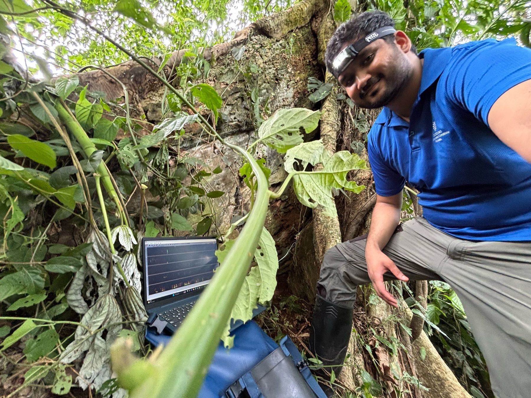 Nakul Wewhare beside a field laptop and recording equipment among dense green vegetation in Panama.